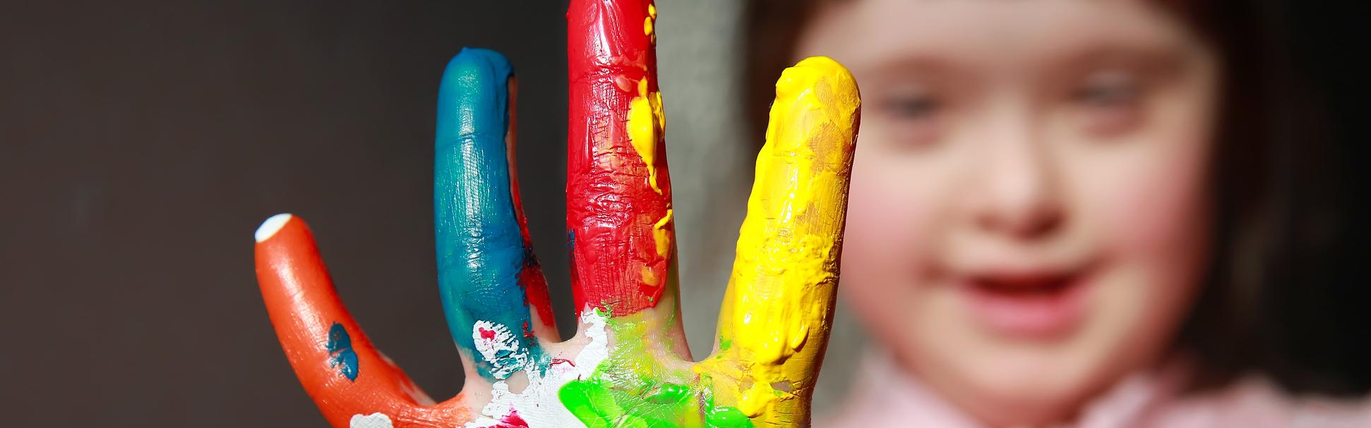 Little girl with Downs Syndrome with multicoloured paint on her hand