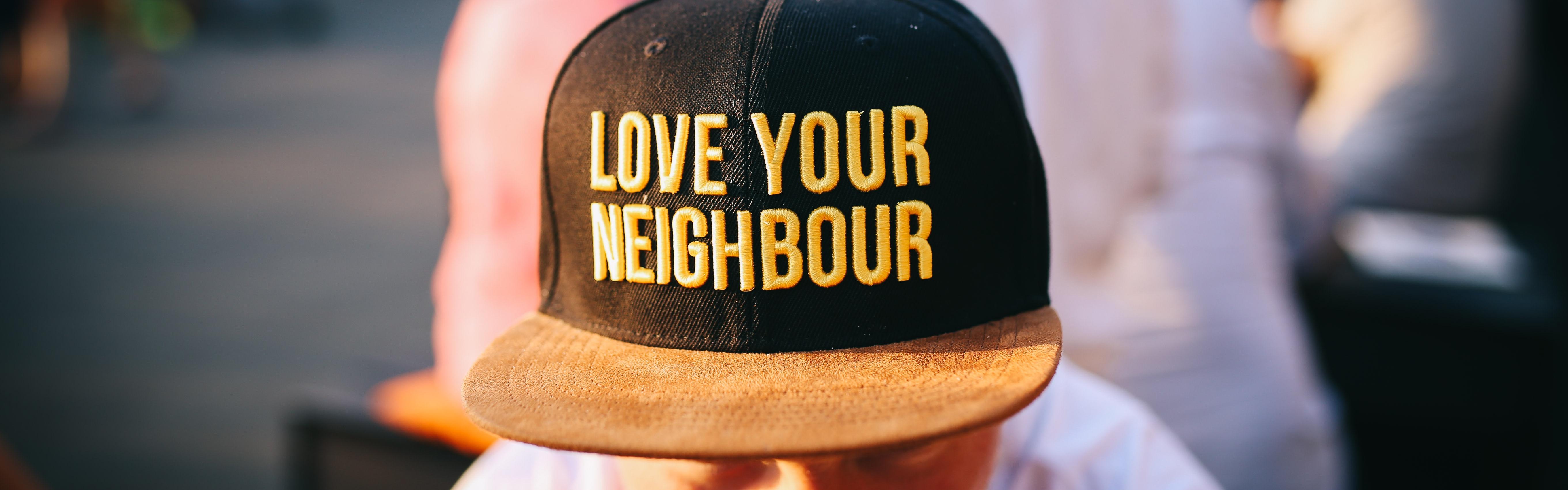 Man sat looking downwards with cap with words 'Love thy Neighbor'