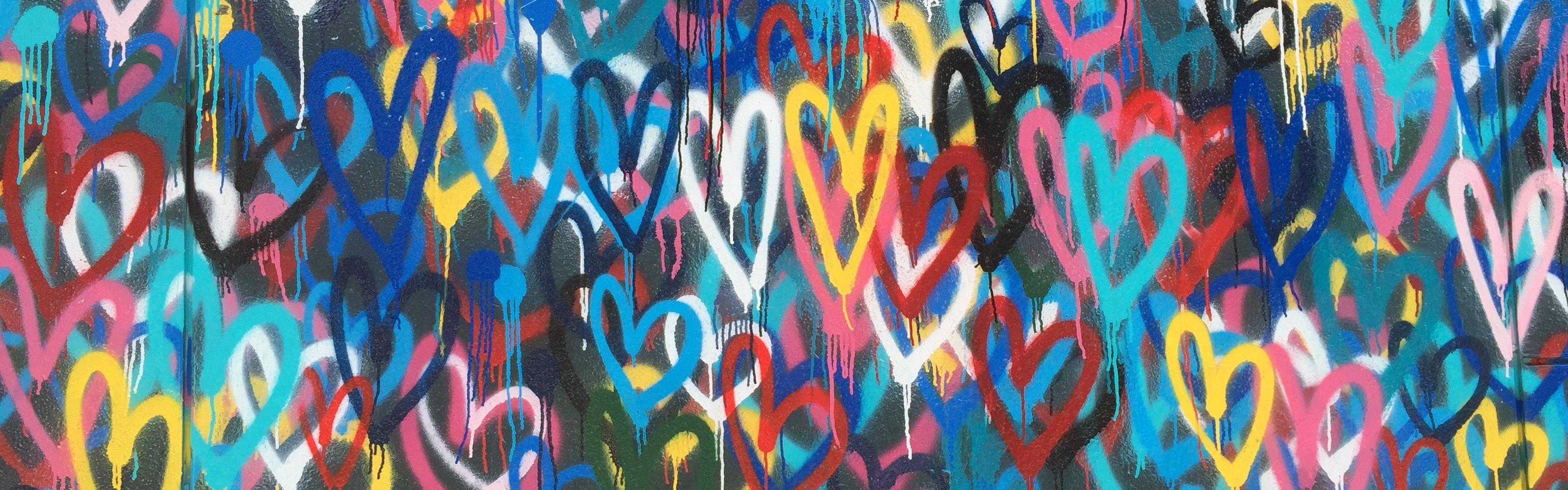 Wall covered in graffitied love hearts in different colours